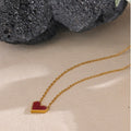 Gold necklace with a red heart pendant on a beige surface.